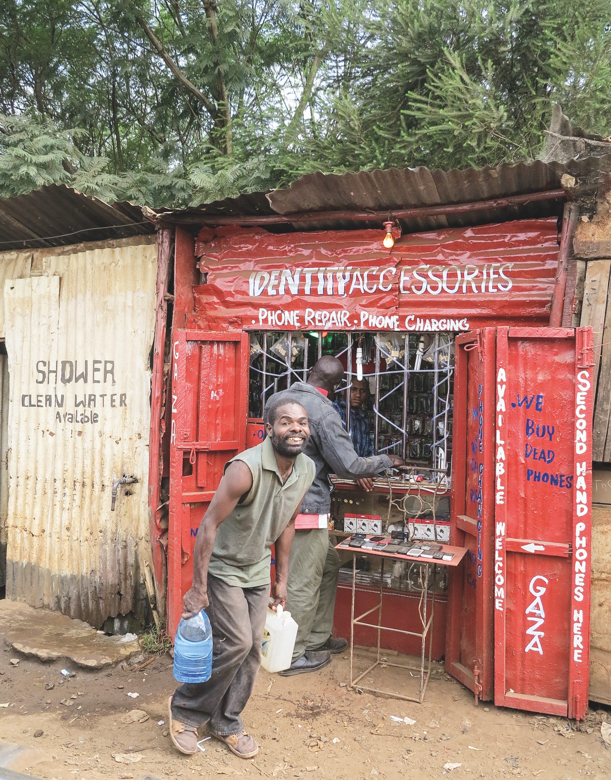 Mies kantaa vettä. Taustalla puhelinliikkeen ikkuna Kiberan slummialueella.
