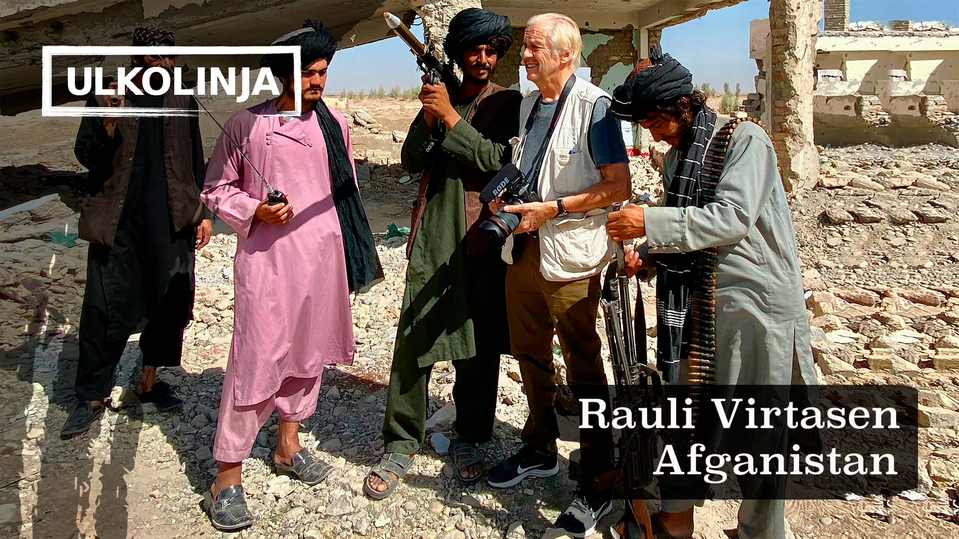 Rauli Virtanen på arbetsuppdrag i Afghanistan. Han står bland talibanerna med kameran i handen. Talibanerna har vapen i sina händer.