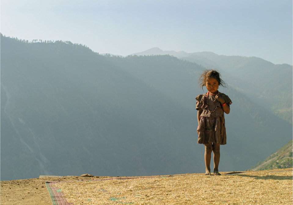 A little girl dressed in a worn dress in a misty mountain landscape.